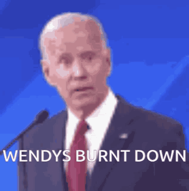 a man in a suit and tie is speaking into a microphone with the words wendy 's burnt down above him .