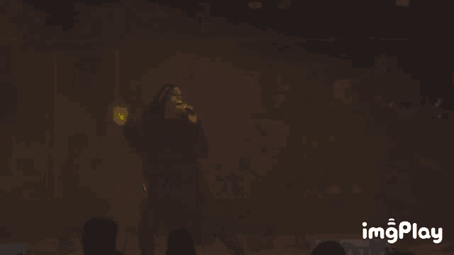 a man singing into a microphone with a yellow light behind him and the word imgplay below him
