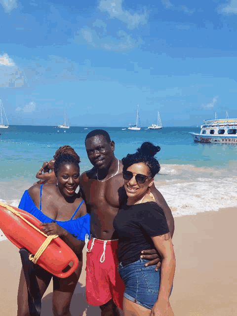 a man and two women pose for a picture on a beach with a boat in the background that says ' pirate ' on it