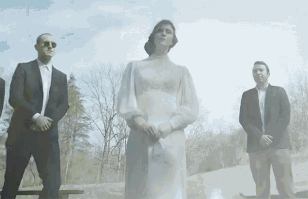 a woman in a white dress is surrounded by men in suits