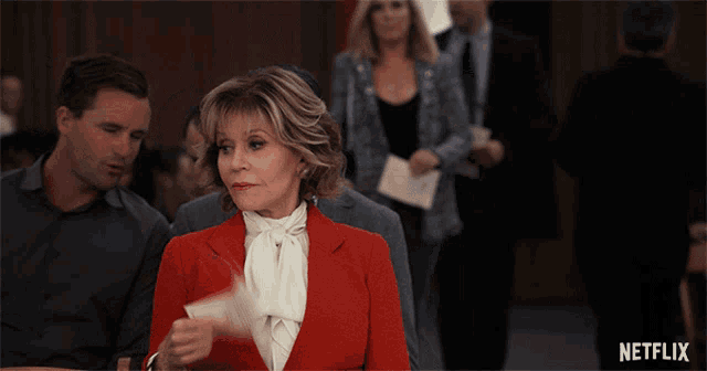 a woman in a red jacket is looking at a piece of paper with a netflix logo in the background