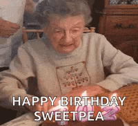 an elderly woman is blowing out candles on a cake .