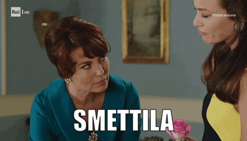 two women are standing next to each other and one of them is holding a pink rose and says smettila