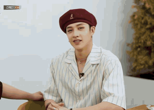 a man wearing a striped shirt and a burgundy beret with kangol on it