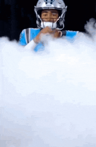 a football player in a helmet is surrounded by white smoke .