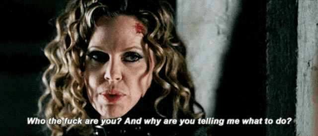 a woman with curly hair is standing next to a wall and says who the fuck are you and why are you telling me what to do