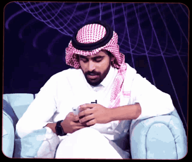 a man wearing a head scarf and a white shirt looks at his phone