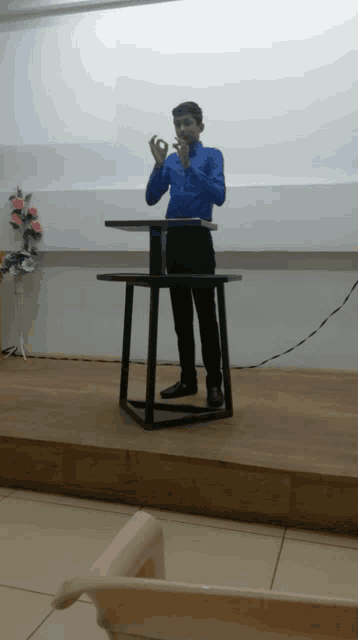 a man in a blue shirt is standing on a wooden stage giving a presentation