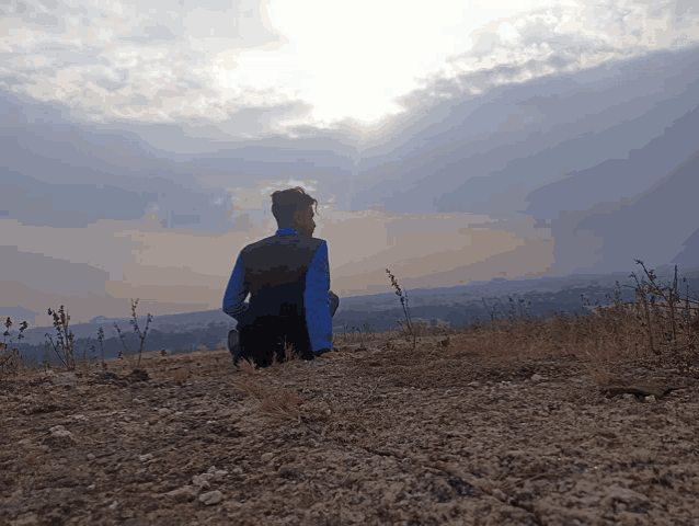 a person sitting on a hill with the sun shining through the clouds behind them