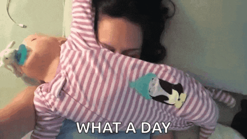 a woman is laying on a bed holding a baby in her arms and says `` what a day '' .