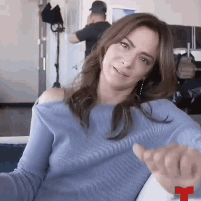 a woman in a blue sweater is sitting on a couch and making a funny face .