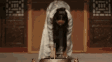 a woman in a white dress is kneeling down in front of a candle burner .
