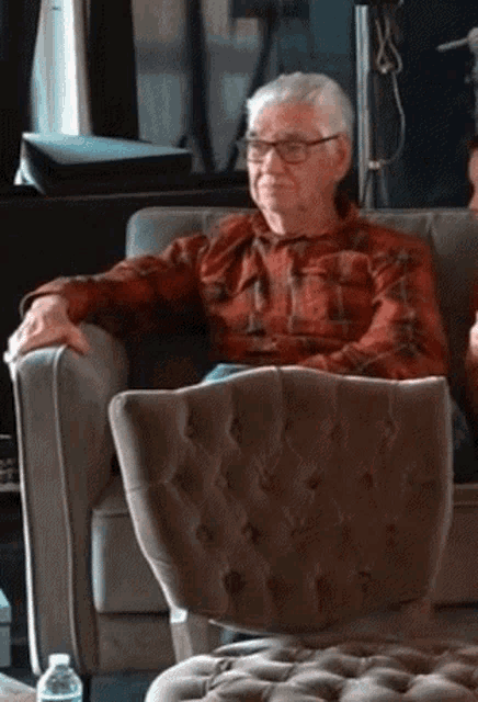 a man wearing glasses is sitting in a chair with his hands on his hips