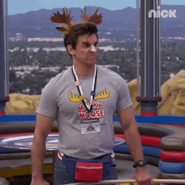 a man wearing a moose headband and a moose t-shirt is standing in front of a table .