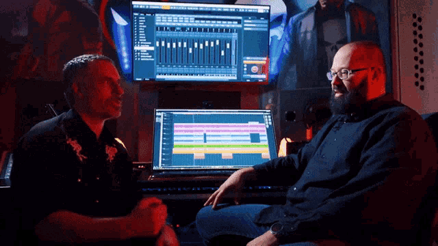 two men are sitting in front of a computer with a skull on the wall