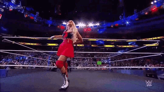 a woman in a red dress is standing in a wrestling ring