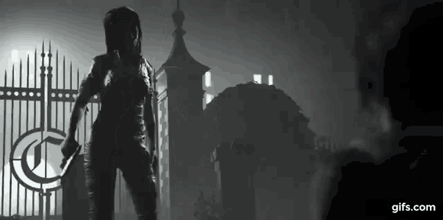a black and white photo of a person holding a sword in front of a fence .