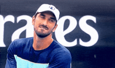 a man wearing a blue shirt and a white hat is smiling in front of a sign that says raes