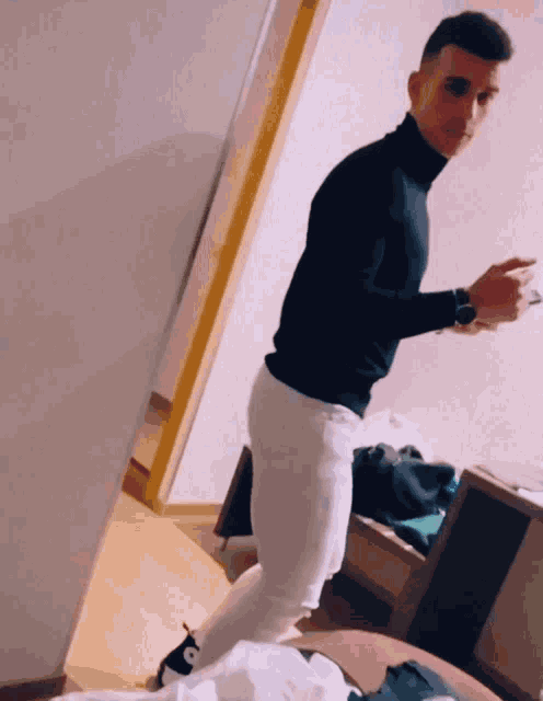 a man wearing a black turtleneck and white pants is standing in a room