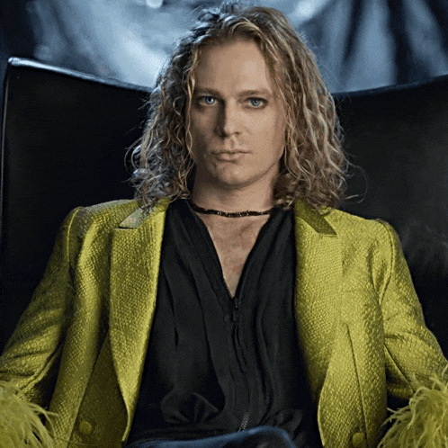 a man with long blonde hair wearing a black shirt and a yellow jacket