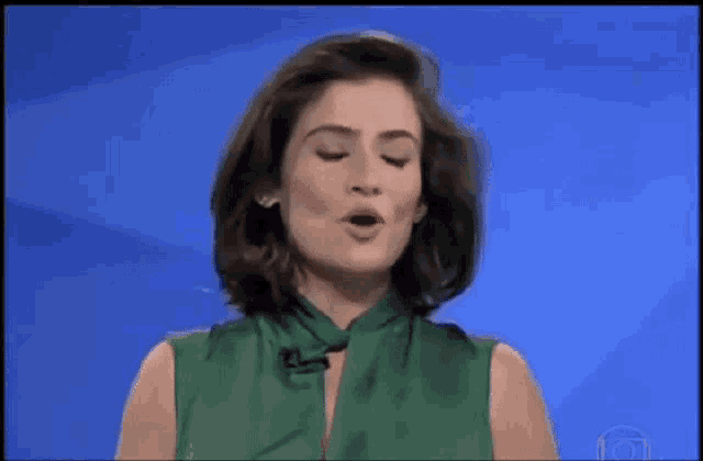 a woman in a green dress is making a funny face while standing in front of a blue background .
