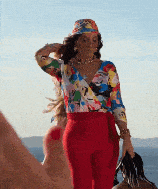a woman wearing a colorful top and red pants is standing on a beach