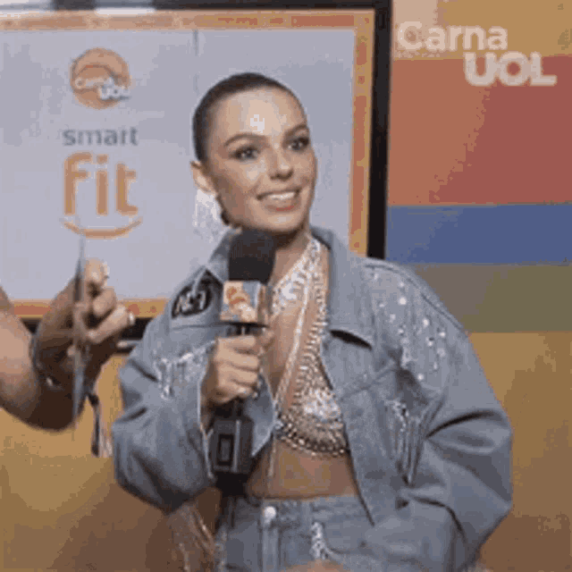 a woman is talking into a microphone while wearing a denim jacket and a bra .
