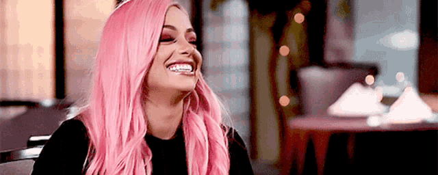 a woman with pink hair is sitting at a table in a restaurant laughing .