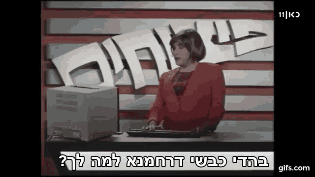 a woman in a red jacket is typing on a keyboard in front of a computer monitor .