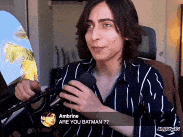 a man in a striped shirt is talking into a microphone and says ambrine are you batman ?