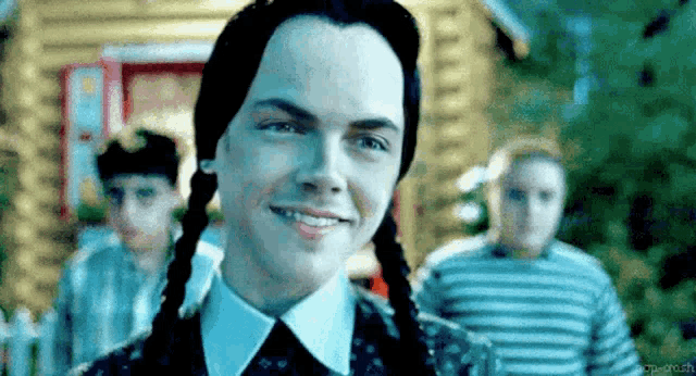a young man with pigtails is smiling in front of a group of children .