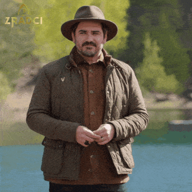 a man wearing a hat and a jacket stands in front of a lake with the word zradci above him