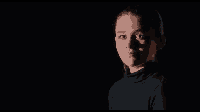 a young girl in a black turtleneck sweater is looking at the camera in the dark .