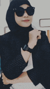 a woman wearing a hijab and sunglasses is standing in front of a sign that says " memories "