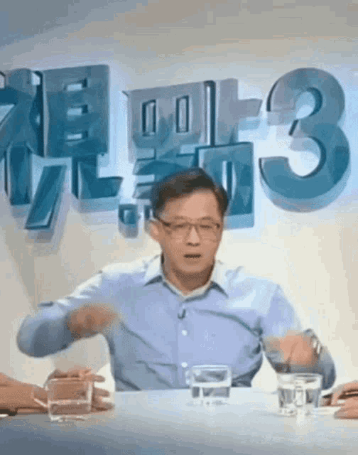a man is sitting at a table with glasses of water in front of a sign that says 3