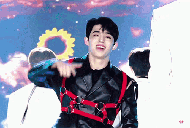 a young man wearing a black leather jacket and red harness is pointing at something