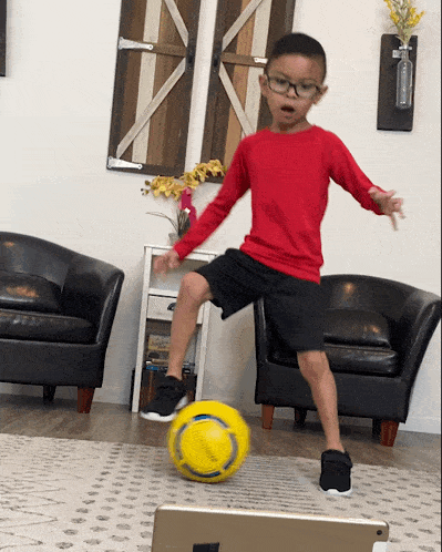 a young boy in a red shirt kicking a yellow ball