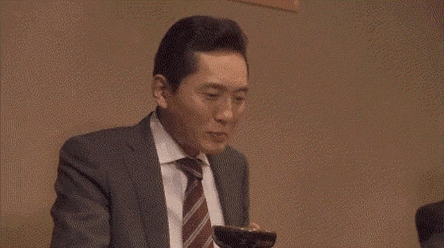 a man in a suit and tie is eating noodles with chopsticks .