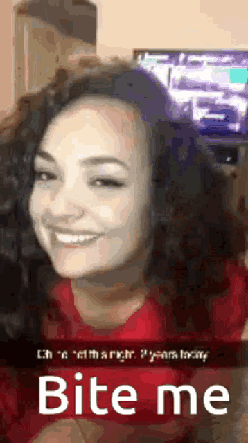 a woman in a red shirt is smiling and looking at the camera with the words bite me below her .