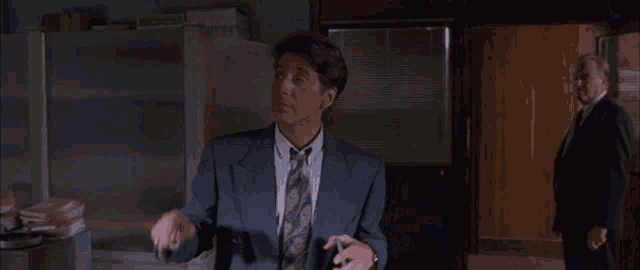 a man in a suit and tie is standing in an office with a man in a suit standing behind him .