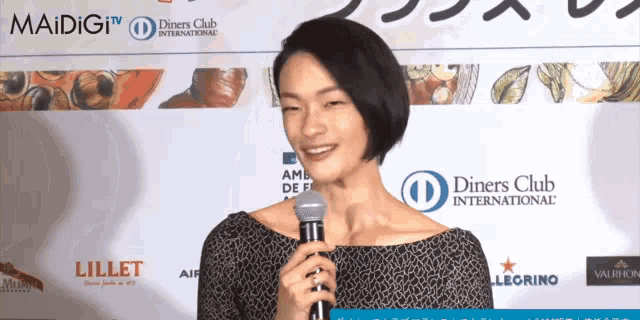 a woman is holding a microphone in front of a diners club international sign