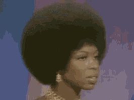 a woman with a very large afro is standing in front of a blue background .