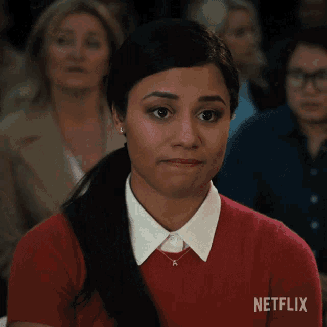 a woman wearing a red sweater and a white collar is sitting in a netflix advertisement