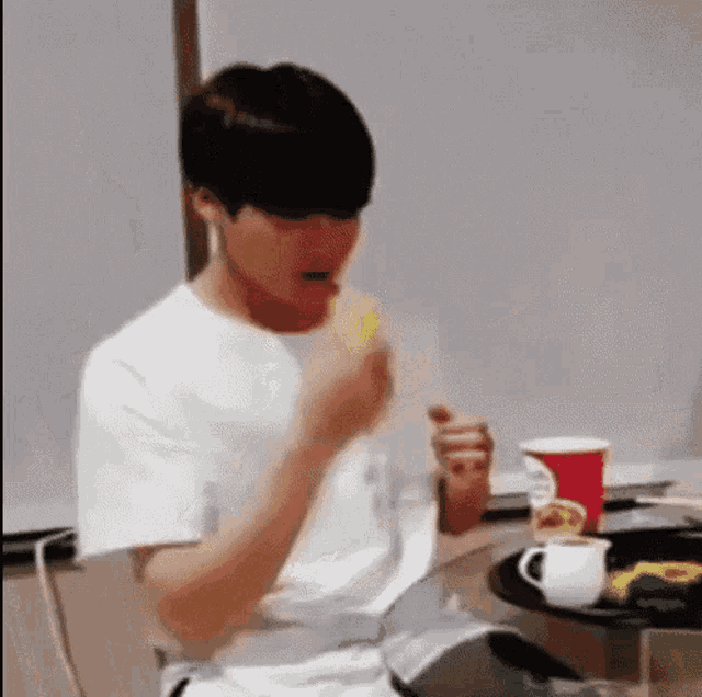a man is sitting at a table eating a banana and drinking a cup of coffee .