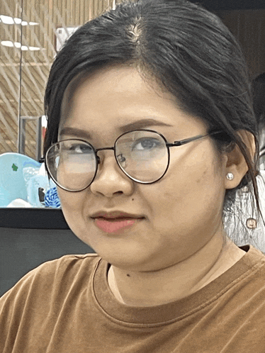 a woman wearing glasses and a brown shirt is smiling