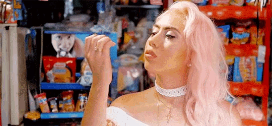 a woman with pink hair is blowing a kiss in front of a candy display .