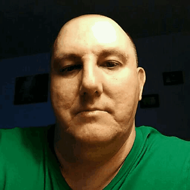 a bald man in a green shirt looks at the camera .