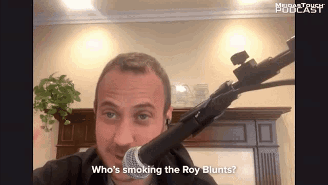 a man speaking into a microphone with the words " who 's smoking the roy blunts " below him