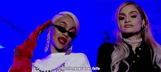two women are standing next to each other on a blue background and one of them is wearing sunglasses .