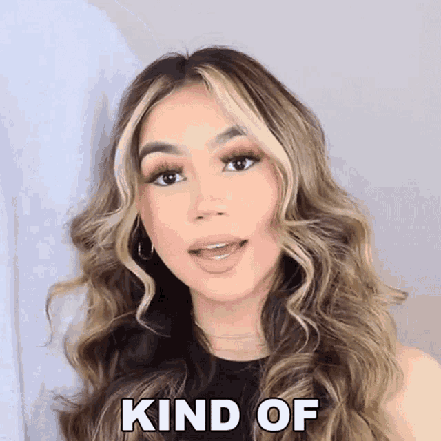 a woman with long wavy hair is making a funny face and the words kind of are above her face .